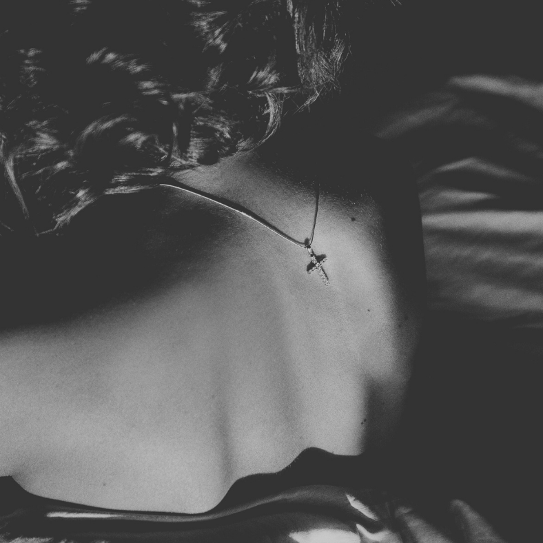 Nu féminin de dos avec des cheveux ondulés et un pendentif visible.